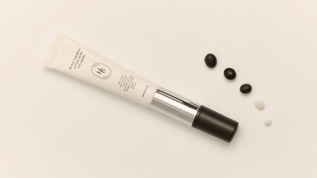 HEVEBLUE Black Yuja Bean Lifting Auto Eye Cream i elegant tub med svarta bönor och två klickar kräm placerade bredvid på beige bakgrund.