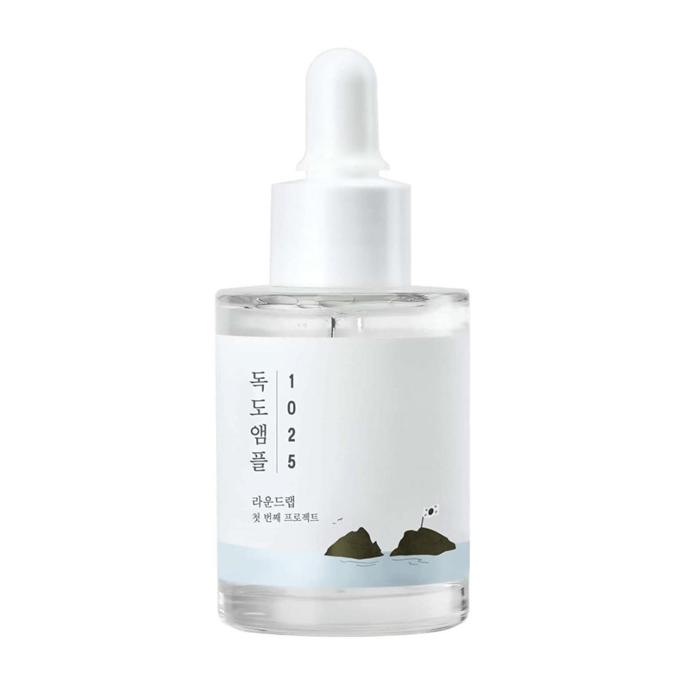 A transparent bottle of 1025 Dokdo Ampoule facial serum, decorated with a minimalist ocean theme, on a white background.