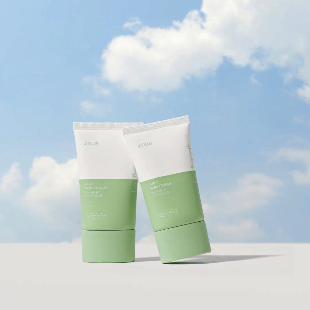 Two tubes of Anua Airy Sun Cream against a sky with white clouds.