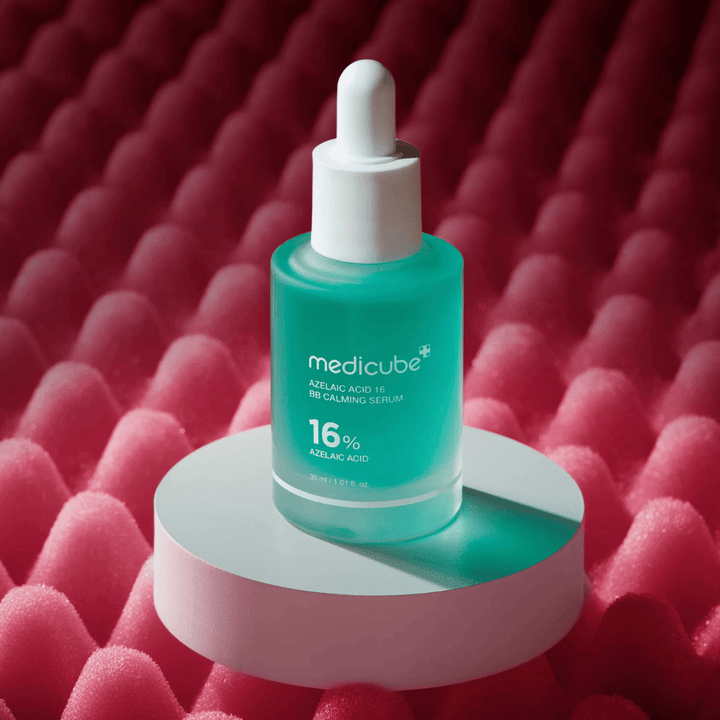 Product image of Medicube Azelaic Acid 16 BB Calming Serum placed on a white podium surface with a pink textured background that highlights the serum’s soothing and skin-improving profile.