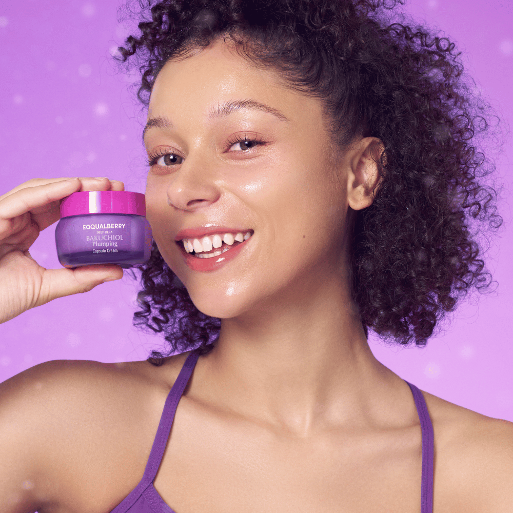 Woman with glowing skin holds EQQUALBERRY Bakuchiol Plumping Capsule Cream and smiles in front of a purple background.