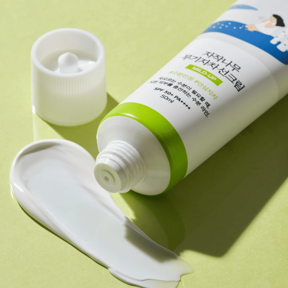 Close-up of Birch Juice Moisturizing Mild Up Sunscreen with unscrewed cap, white sunscreen smeared on a light green background, SPF 50+ PA++++, 50 ml.