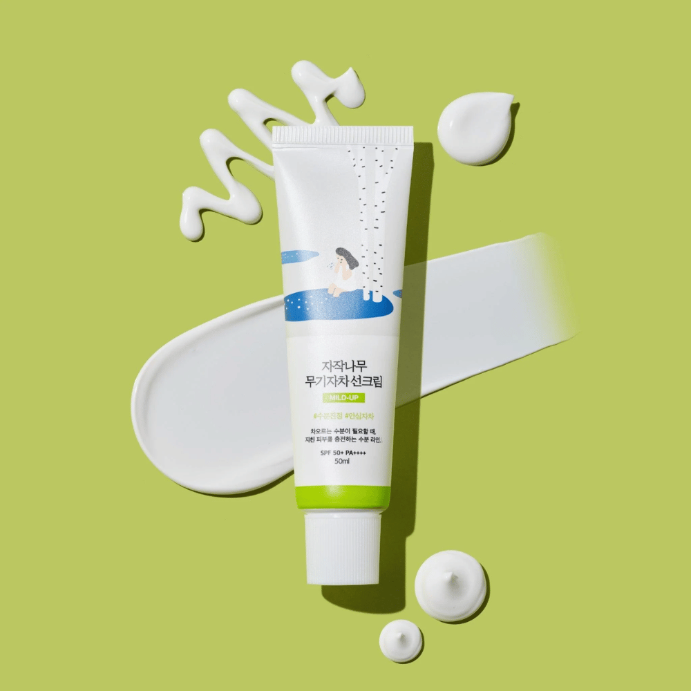 Birch Juice Moisturizing Mild Up Sunscreen – white tube with a green base on a green background, surrounded by smeared sunscreen and drops, SPF 50+ PA++++, 50 ml.