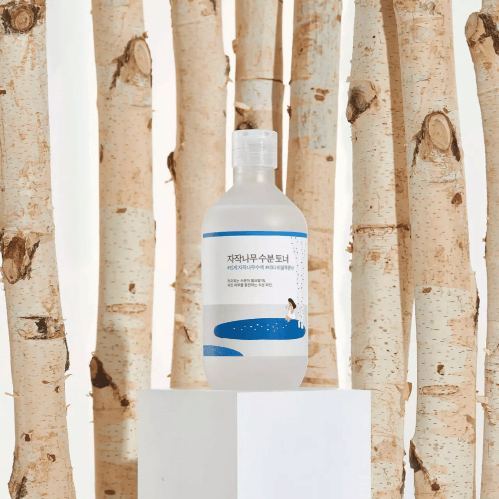 Toner bottle placed in front of several birch trunks and standing on a white cube