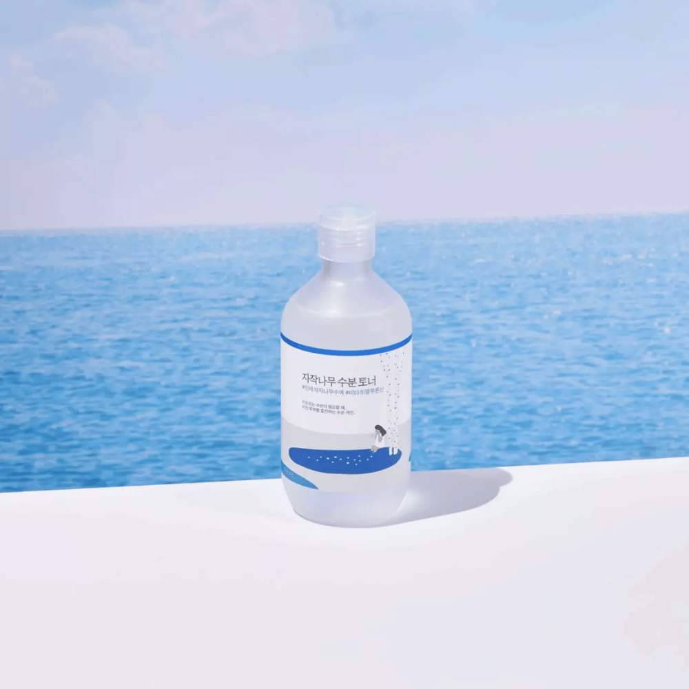 Bottle of ROUND LAB Birch Juice Moisturizing Toner standing on a white surface with the sea and blue sky in the background
