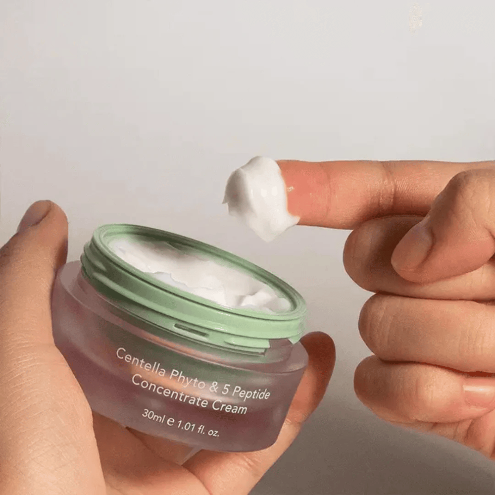 Hand taking a dab of Centella Phyto & 5 Peptide Concentrate Cream from a jar.