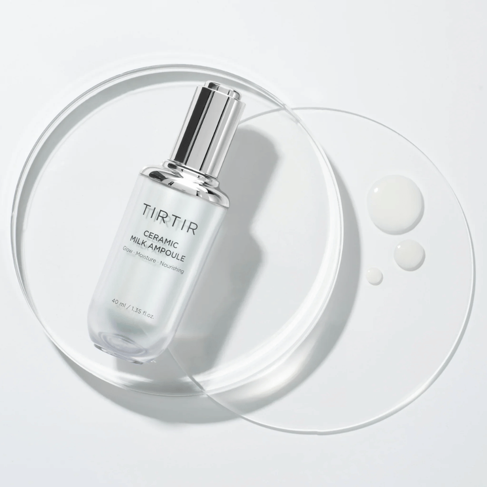 A transparent bottle TIRTIR Ceramic Milk Ampoule on a glass plate with drops, against a white background, highlights glow, moisture, and nourishment.