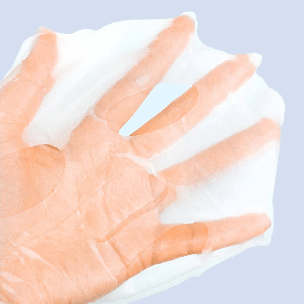 A transparent and moist face mask is held up on a hand against a light blue background. The mask is designed to cover the face with spaces for eyes and mouth.
