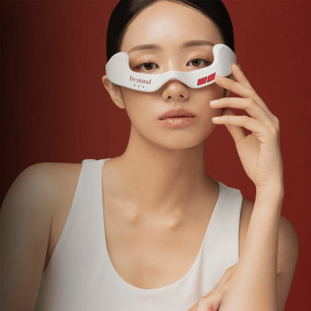 Model image where a person is using Beaund Eye Rejuv, a futuristic LED device for the area around the eyes, against an elegant red background.