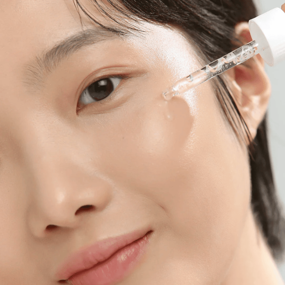 Close-up of woman applying serum on cheek with pipette – skincare that provides glow and hydration.