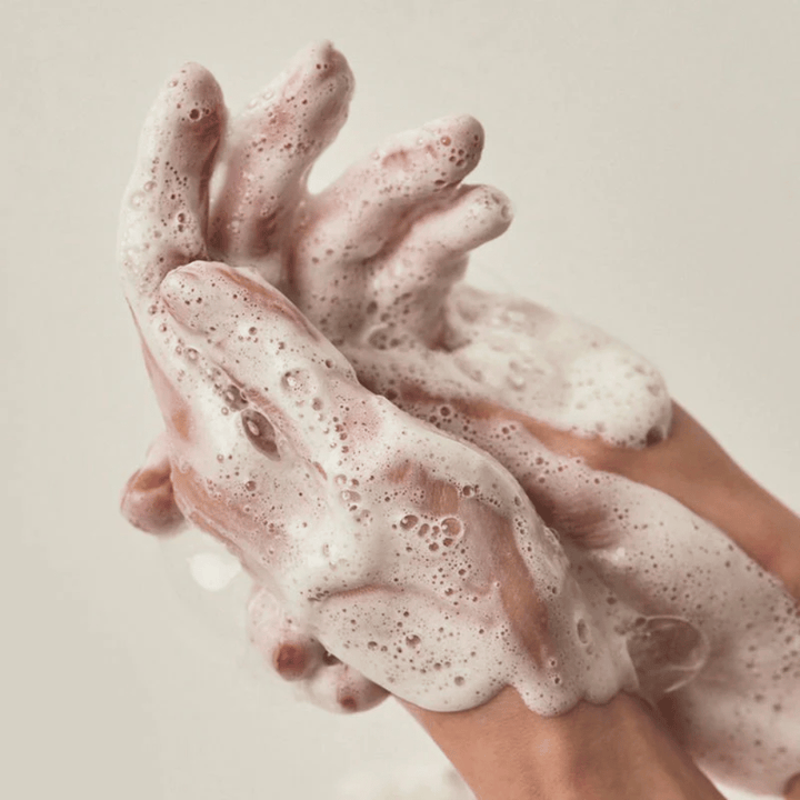 Close-up of hands covered in a rich and creamy cleansing foam. The image illustrates the product's lather and cleansing properties and provides a clear sense of use and texture.