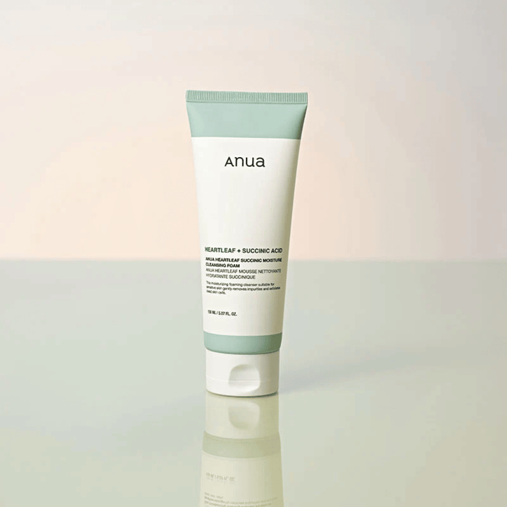 Standalone product image of Anua Heartleaf + Succinic Acid Moisture Cleansing Foam. The product is shown standing on a reflective surface that clearly highlights the packaging design and the brand's sleek aesthetic.