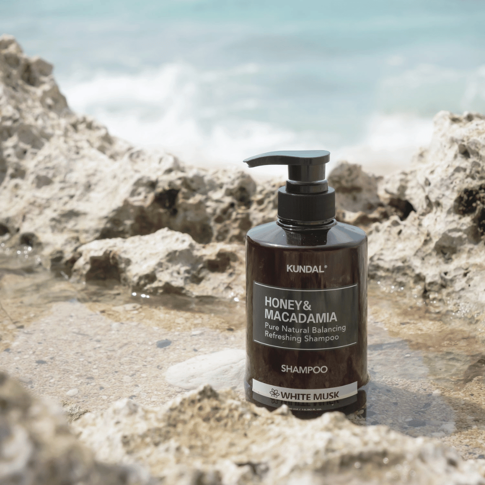 KUNDAL Honey & Macadamia Nature Shampoo White Musk placed on rocks by the sea, a natural hair care product with a fresh scent.