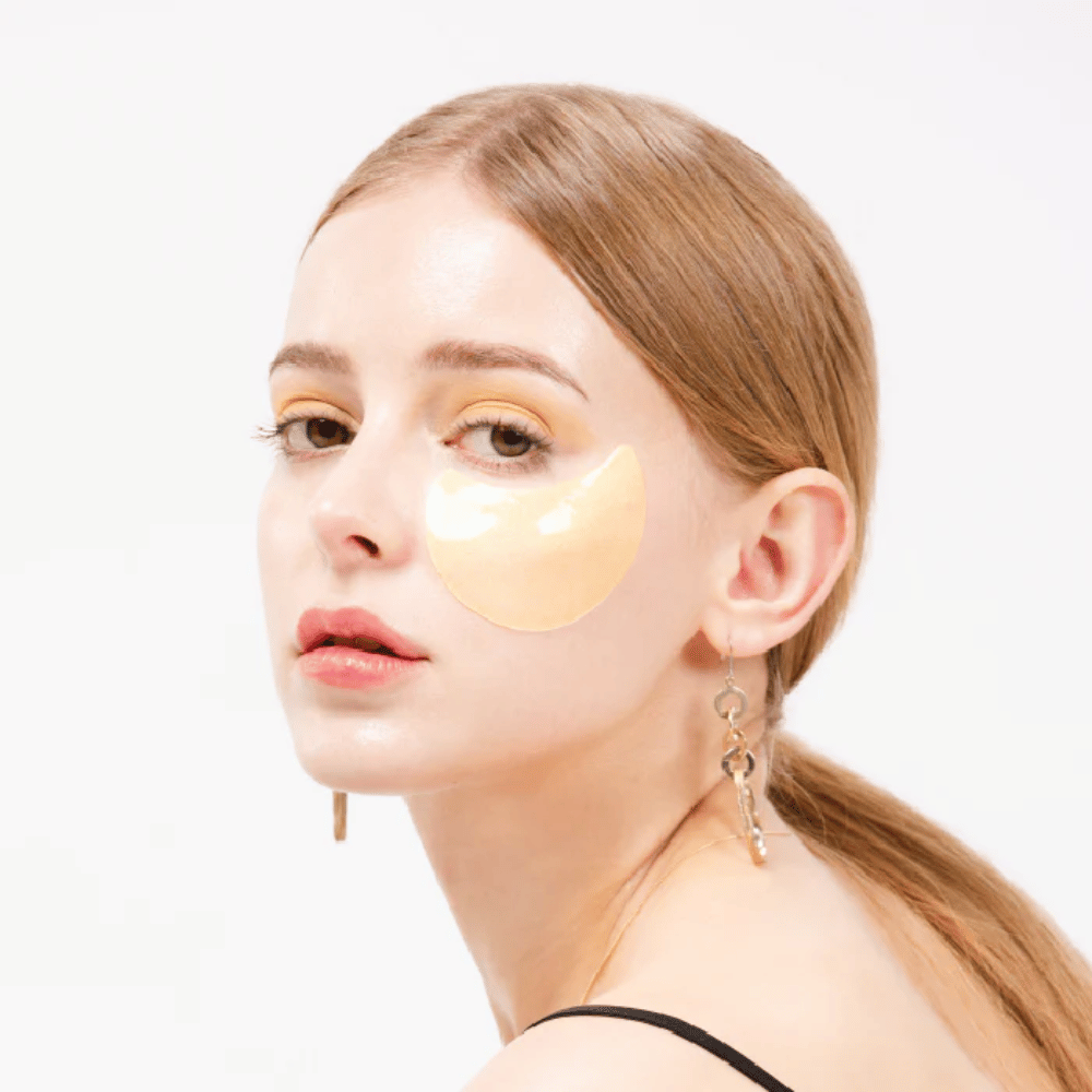 Model wearing a gold shimmering hydrogel eye patch under the eye for a radiant effect.