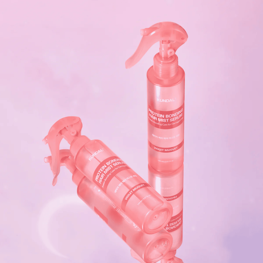 KUNDAL Protein Bonding Hair Mist Serum Violet Muguet in pink spray bottles, standing and lying against a light pink background with reflection.
