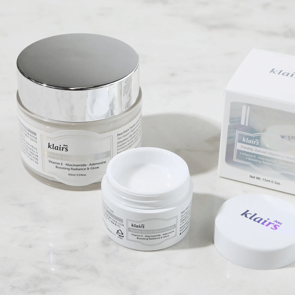 A collection of skincare products from Klairs on a marble bench: a closed jar, an open jar with cream, and a box with text.