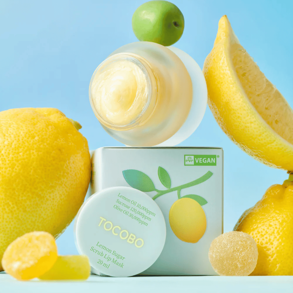 Jar with Tocobo Lemon Sugar Scrub Lip Mask placed among lemons and packaging, marked as vegan-friendly.
