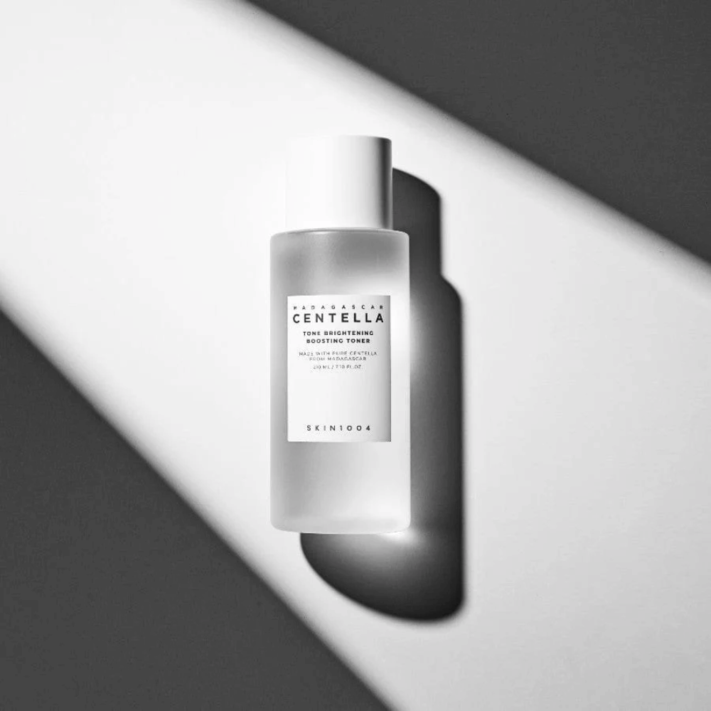 Bottle of SKIN1004 Madagascar Centella Tone Brightening Boosting Toner  lying on a white surface with dramatic shadow in black and white light play.