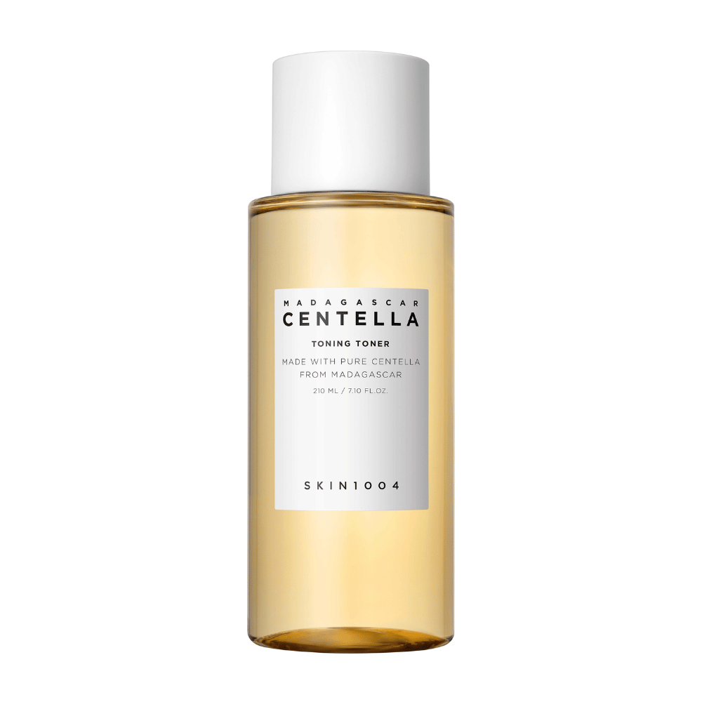 The image shows a bottle with skincare toner, labeled "Madagascar Centella Toning Toner" from SKIN1004. The product is stated to contain 210 ml or 7.10 fl.oz and is made with pure Centella from Madagascar. The packaging is simple and elegant with a transparent bottle and golden-toned liquid inside, giving a sense of luxury and purity. The brand's logo SKIN1004 is clearly visible at the bottom of the label.