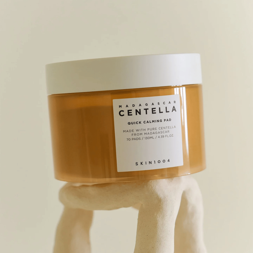 Jar with SKIN1004 Madagascar Centella Quick Calming Pad placed on a sculpture-like white pedestal – amber-colored container with white label and lid.