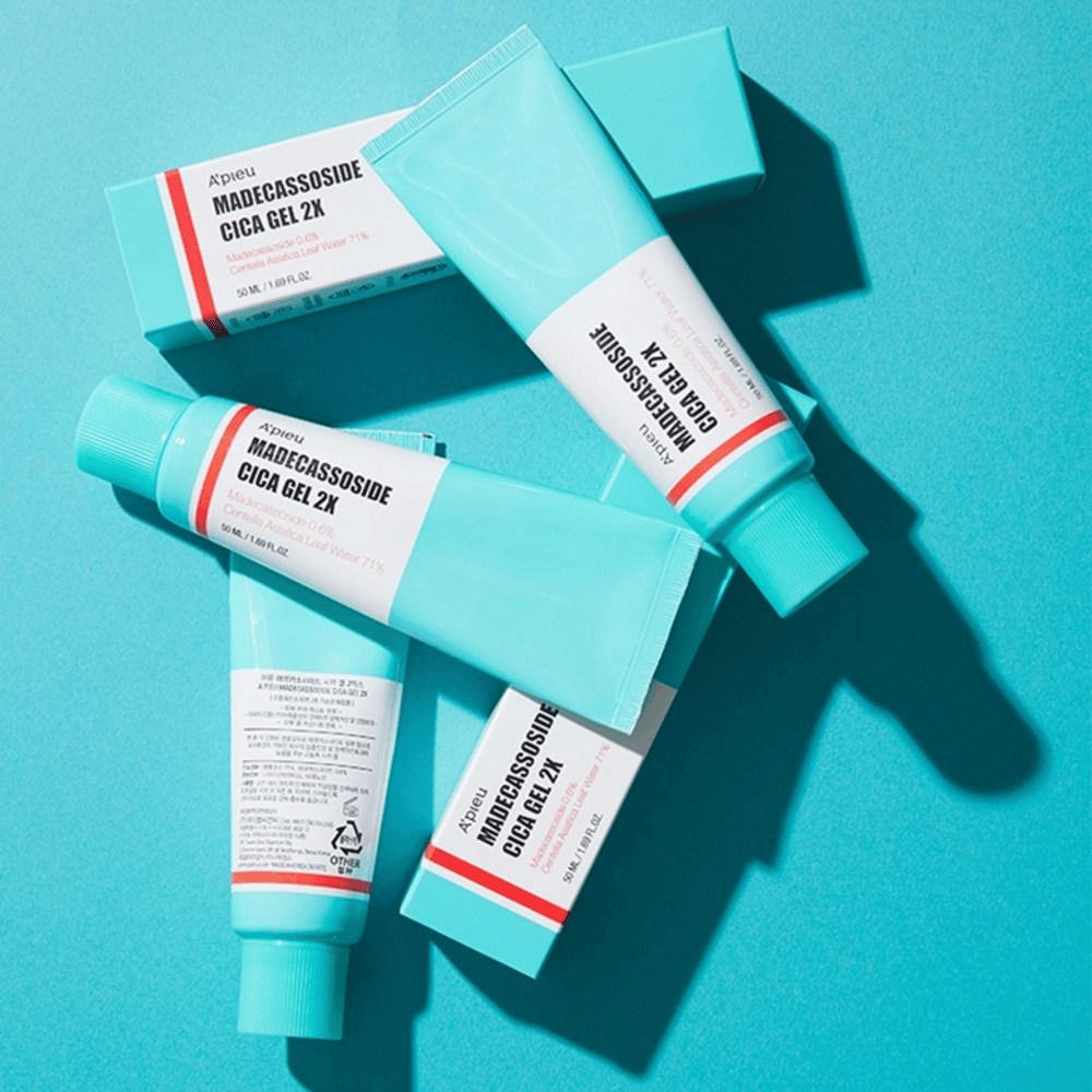 Several tubes and boxes of A'pieu Madecassoside Cica Gel 2X in turquoise packaging with white and red labels, lying against a turquoise background in strong light.