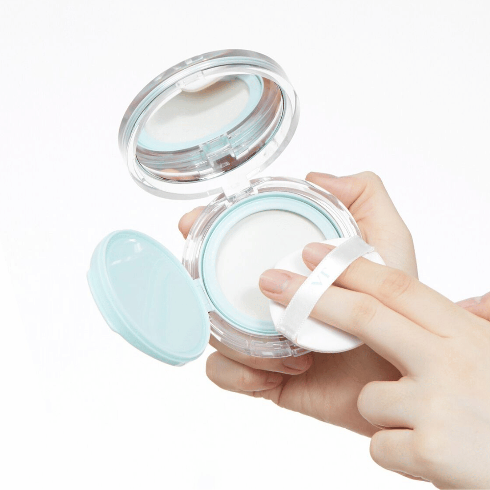 A hand holds an open jar with VT PDRN Essence Glow Sun Pact. The puff is about to apply the powder, which has a white surface and a blue edge around the jar.