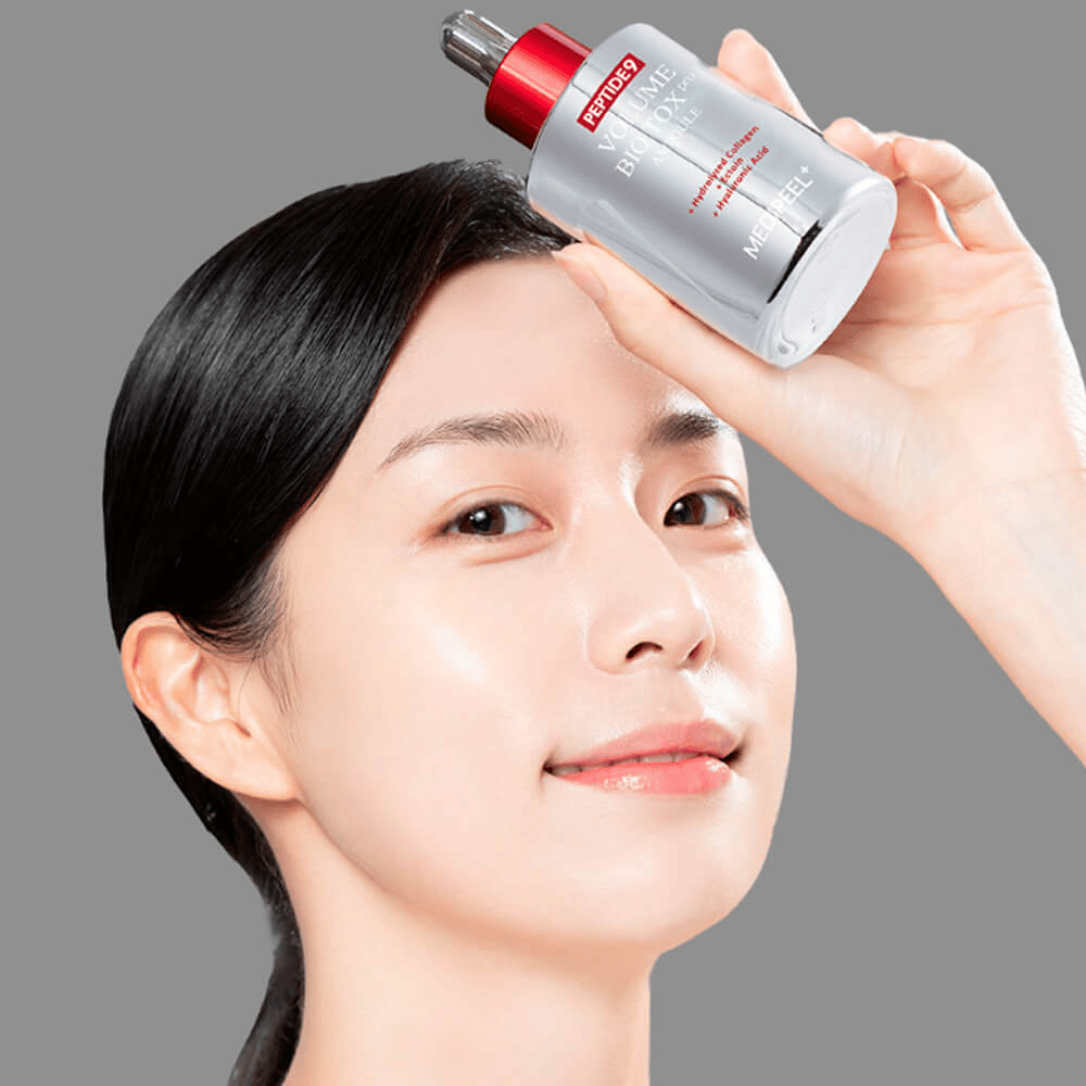 Person holding up MEDI-PEEL Peptide 9 Volume Bio Tox Pro Ampoule to the forehead. The skin looks hydrated and radiant – the serum enhances elasticity and firmness.