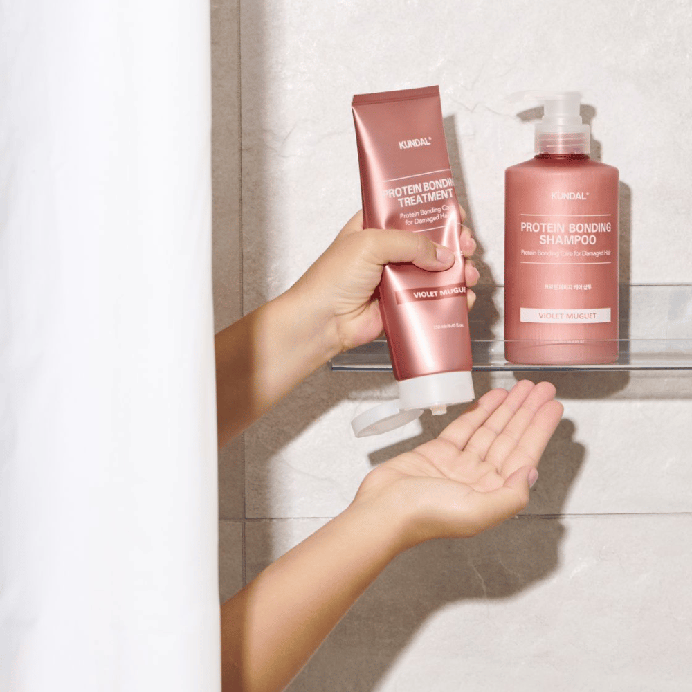 KUNDAL Protein Bonding Treatment Violet Muguet is used in the shower, with Protein Bonding Shampoo placed on the shelf next to it.