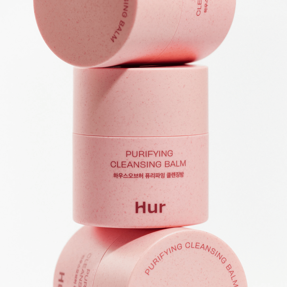 How Purifying Cleansing Balm in pink packaging stacked in studio. Cleansing balm that effectively dissolves makeup, oil, and impurities without drying out the skin.