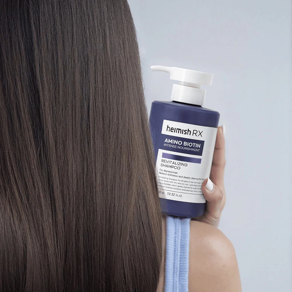 Heimish RX Amino Biotin Revitalizing Shampoo held in hand against long, shiny hair – shows the result of intensive nourishment and hydration for dry hair.