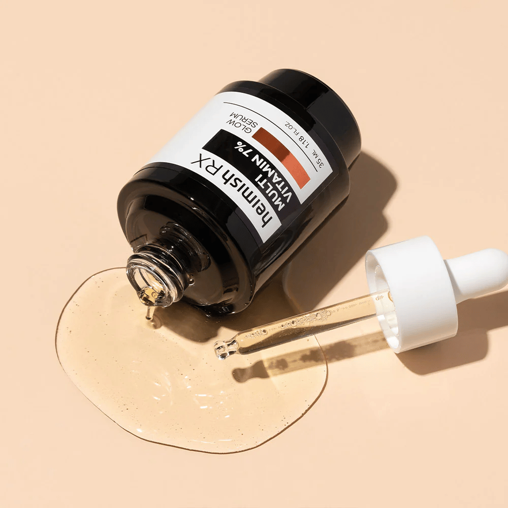 Heimish RX Multi Vitamin 7% Glow Serum lying on a beige background with serum spread around the bottle and a dropper filled with the product, highlighting its nutrient-rich formula.