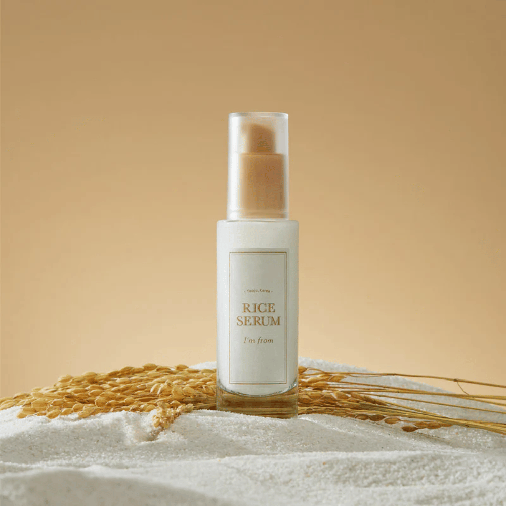 Bottle with "I'm from" Rice Serum, surrounded by rice grains and rice ears against a warm background.