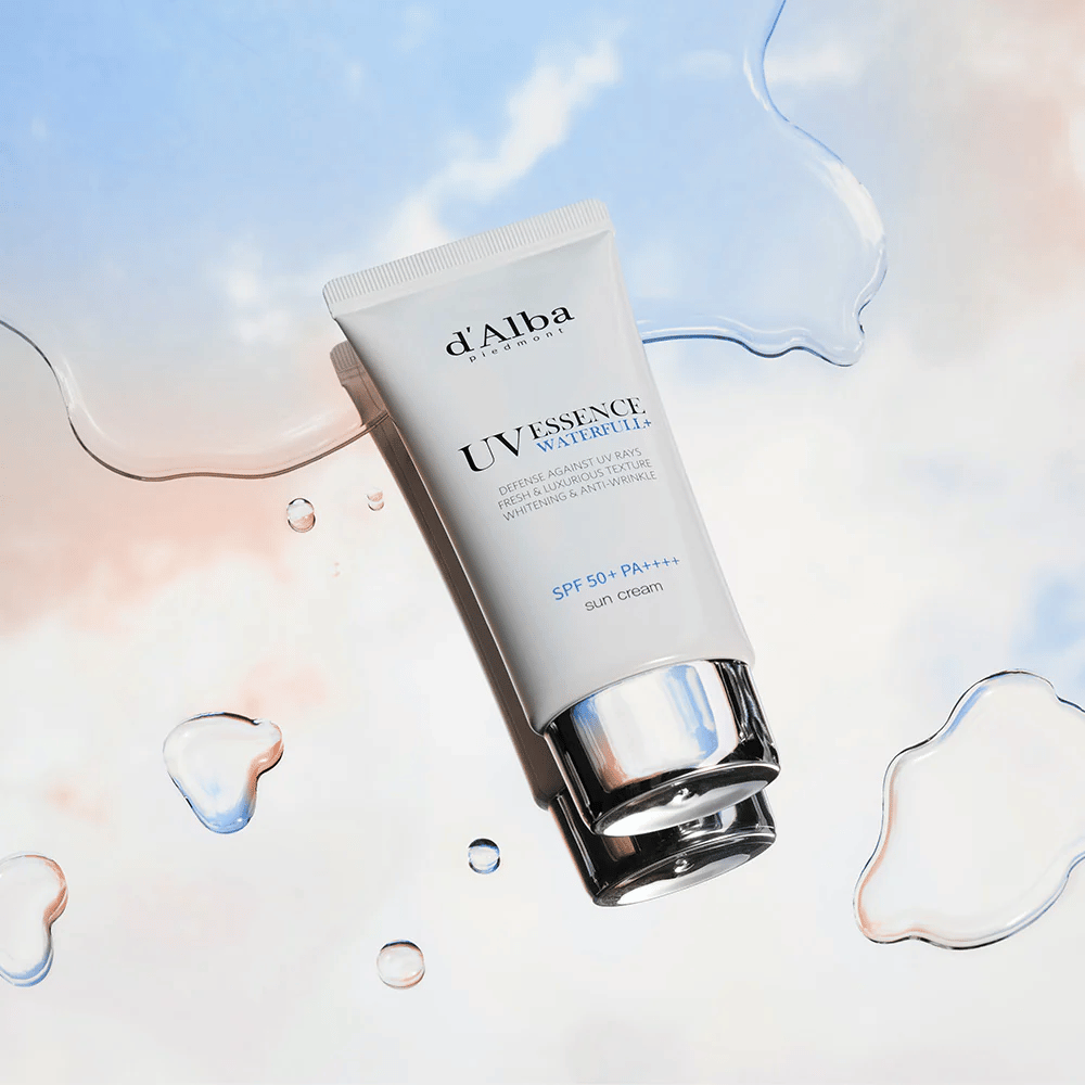 Product image of d'Alba UV Essence Waterfull+ Sun Cream with SPF 50+ PA++++, placed against a background with water splashes and a blue-pink sky – symbolizes light and moisturizing sun protection.