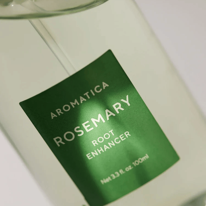 Close-up of the label on AROMATICA Rosemary Root Enhancer. The green label and the transparent bottle highlight the product's clean and minimalist appearance.