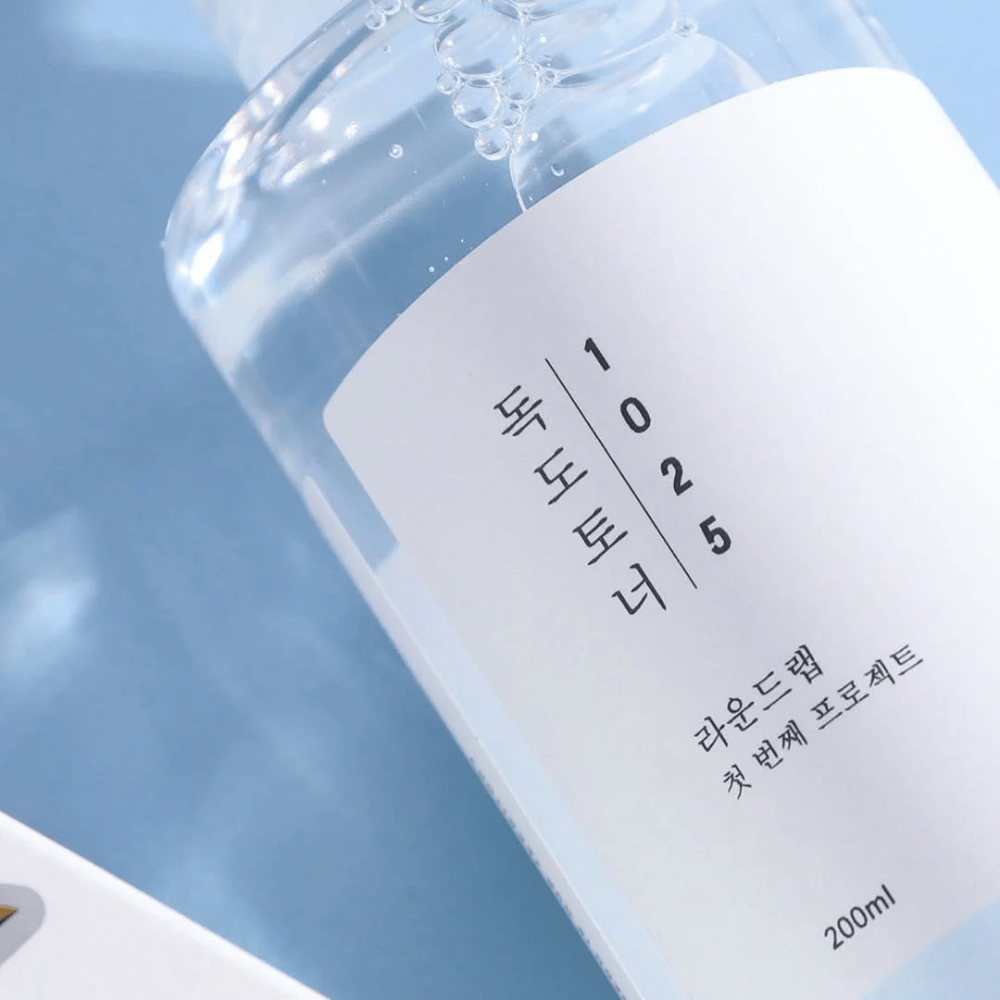 Close-up of a transparent bottle Round Lab 1025 Dokdo Toner, filled with clear liquid, against a blue background.