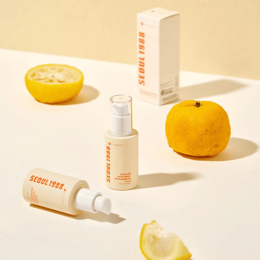 Several bottles and packages of Seoul 1988 Glow Serum arranged with whole and halved yuja fruits in the background.