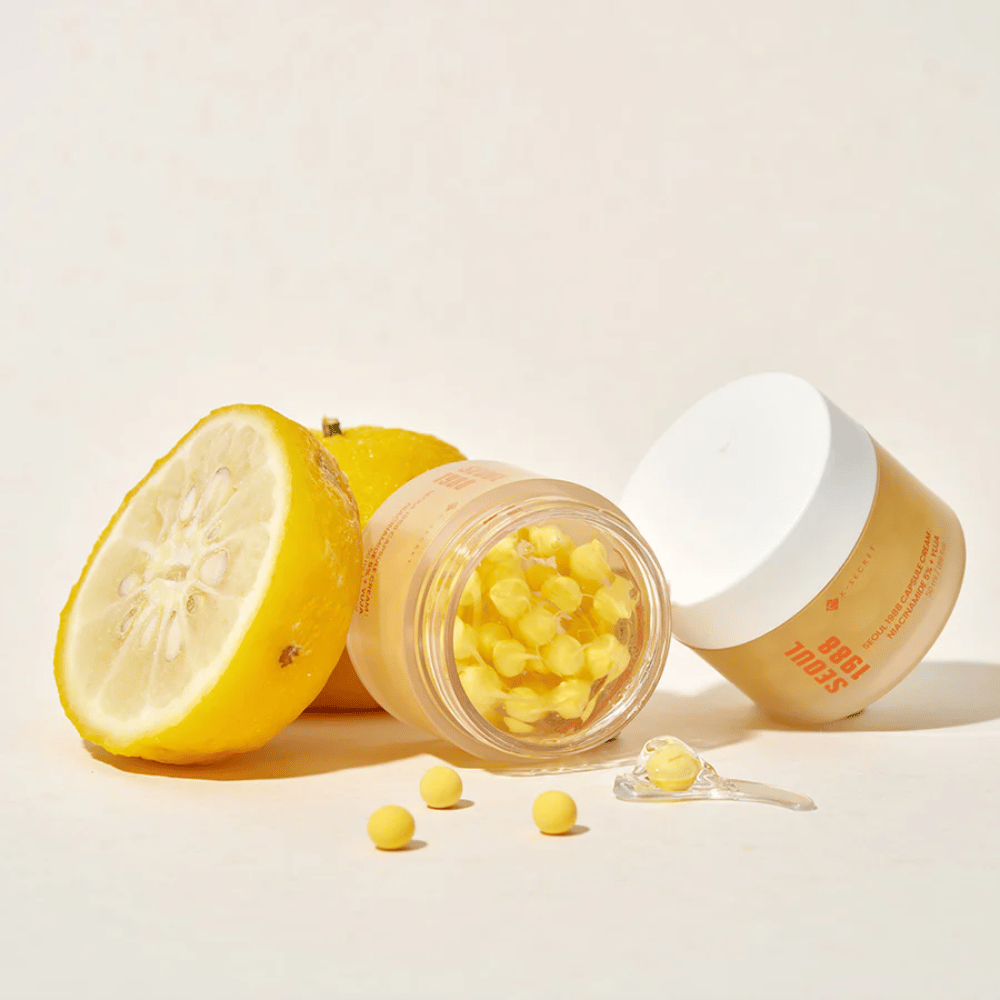 Open jar with yellow capsules next to halved yuja fruit highlighting vitamin C-rich formula.