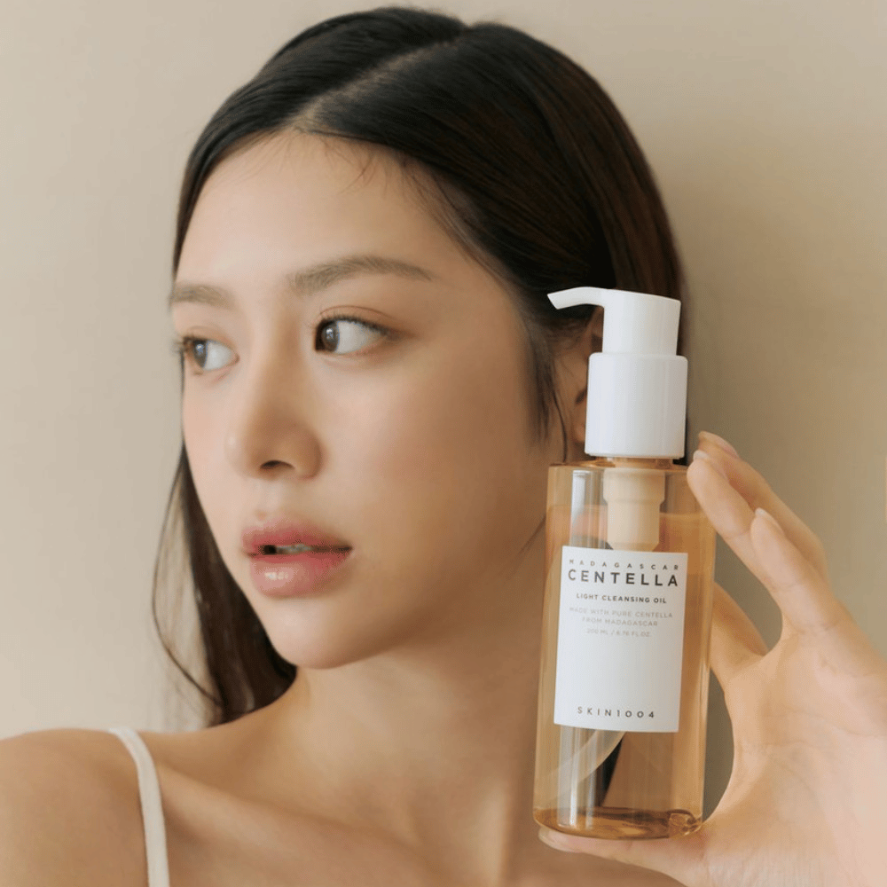 A woman holding up a bottle of SKIN1004 Madagascar Centella Light Cleansing Oil 200 ml facial cleanser.
