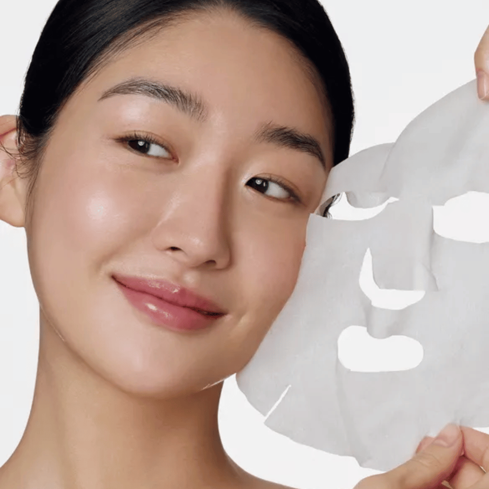 The image shows a person using a face mask, specifically a "Retinol Intense Daily Mask" from Some By Mi. The mask is designed for daily use and contains retinol to improve skin texture, reduce fine lines, and provide a more even skin tone.