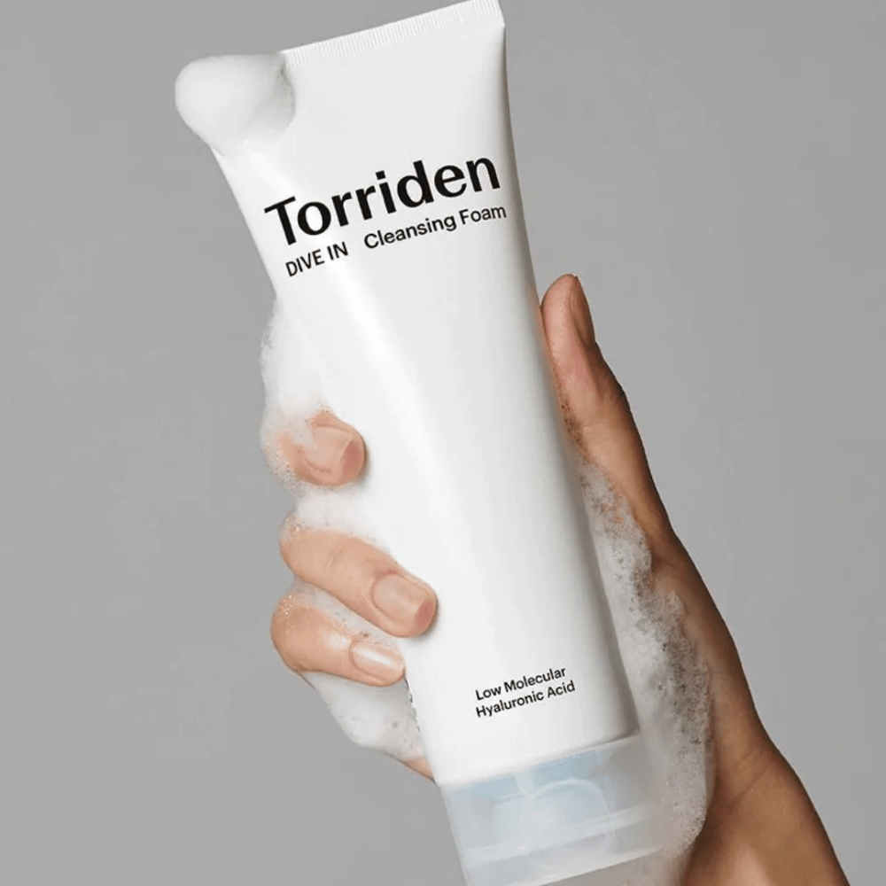 A hand holding a tube pH-balanced Torriden DIVE-IN Low Molecular Hyaluronic Acid Cleansing Foam 150ml.