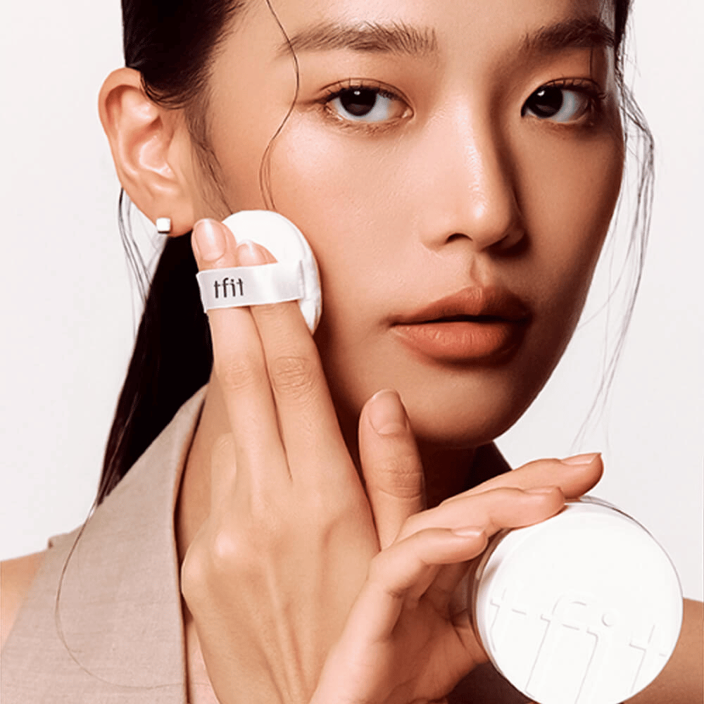 Woman applying TFIT Translucent Set Finishing Powder #02 Skin Beige with a puff, holding a white powder jar with TFIT logo.