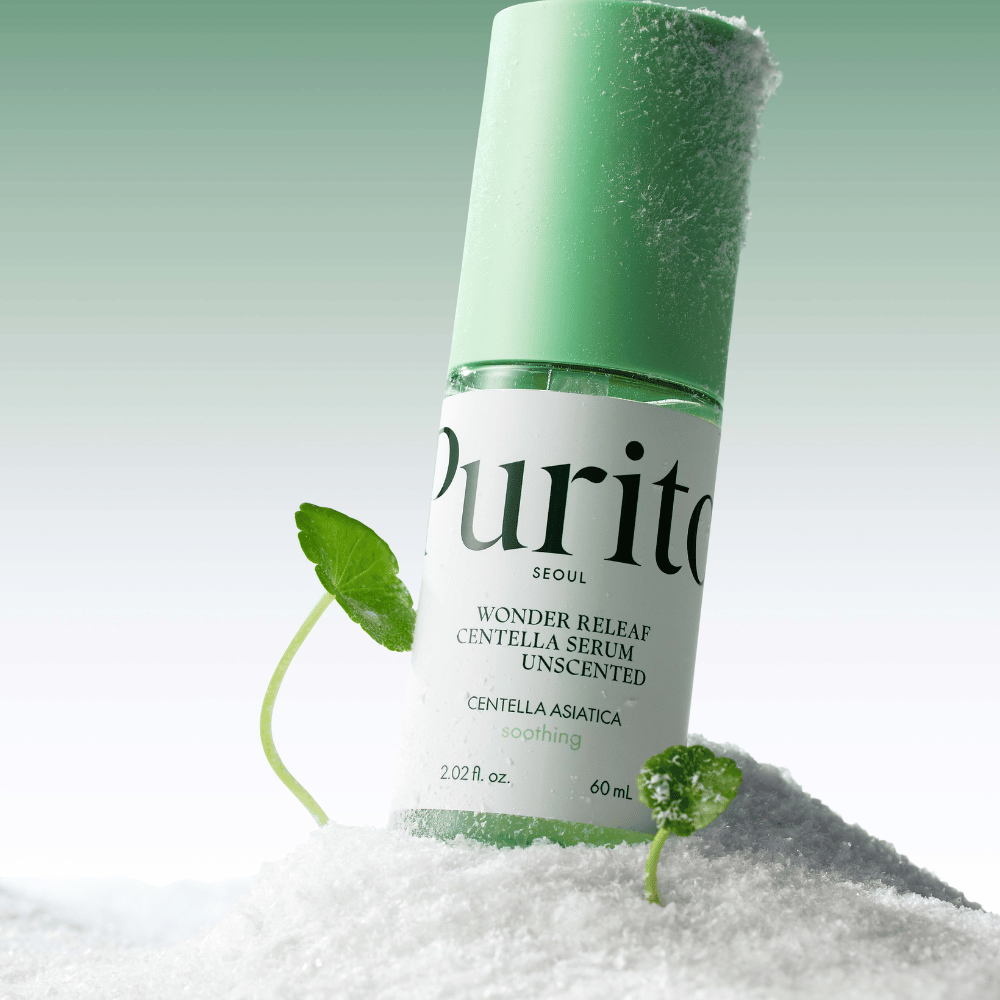 Bottle with Purito Centella Serum lies in snow, green leaves visible, against a soft green background.