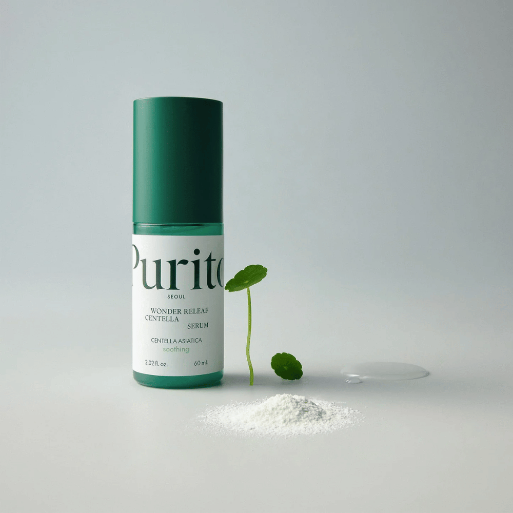 Green bottle of Purito Wonder Releaf Centella Serum 60 ml stands on a white surface, surrounded by centella leaves, a transparent serum drop, and a small white powder.