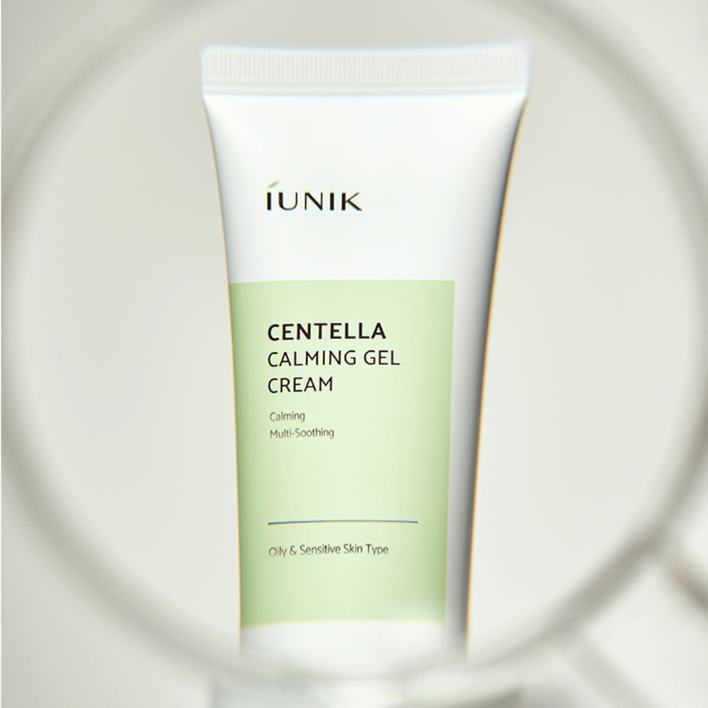 A tube iUNIK Centella Calming Gel Cream with white and light green design stands upright, seen through a round magnifying glass-like frame.