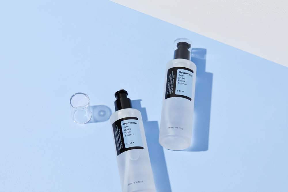 COSRX's Hyaluronic Acid Hydra Power Essence 100ml provides moisturizing benefits on blue surface.