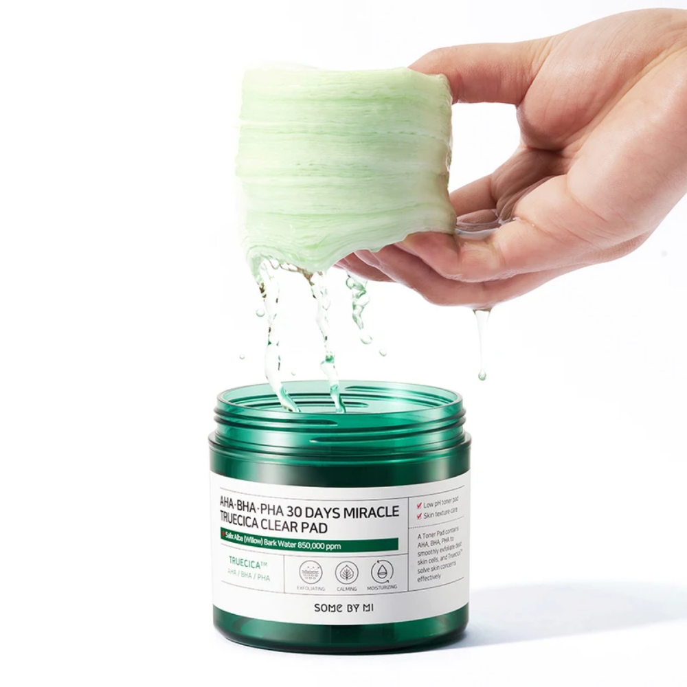 A hand pours a green liquid into a jar for SOME BY MI:s AHA, BHA, PHA 30 Days Miracle Truecica Clear Pad 70 pcs acne outbreak treatment.