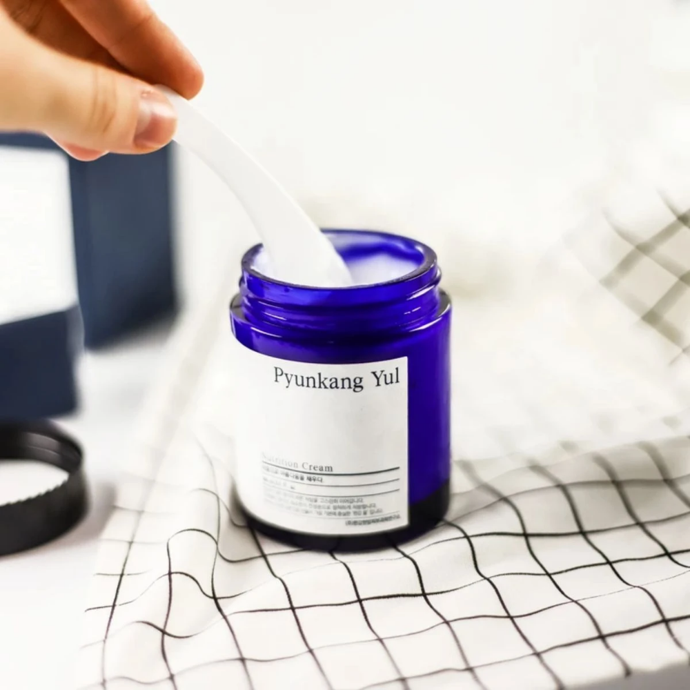 A person uses a jar Pyunkang Yul Nutrition Cream 100ml on a table.