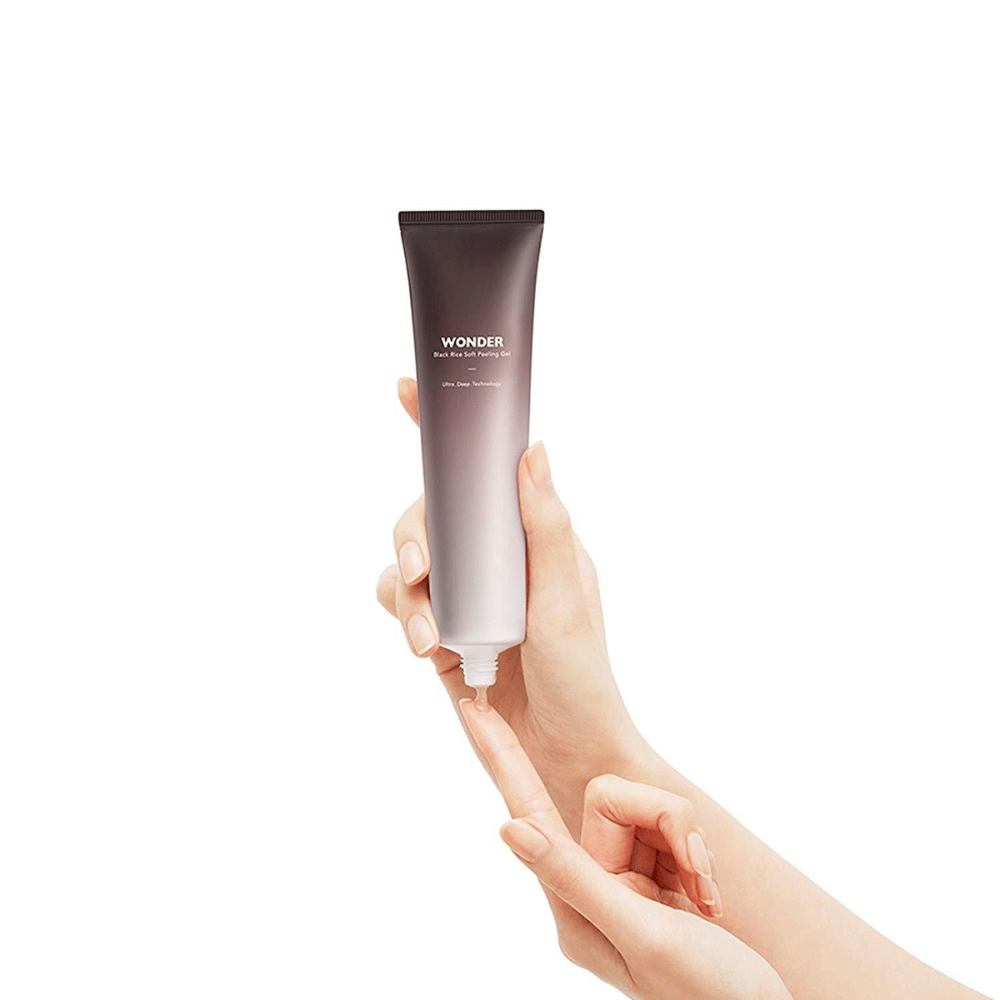 A woman's hand holding a tube of Haruhuru Wonders Black Rice Soft Peeling Gel 100 ml on a white background.