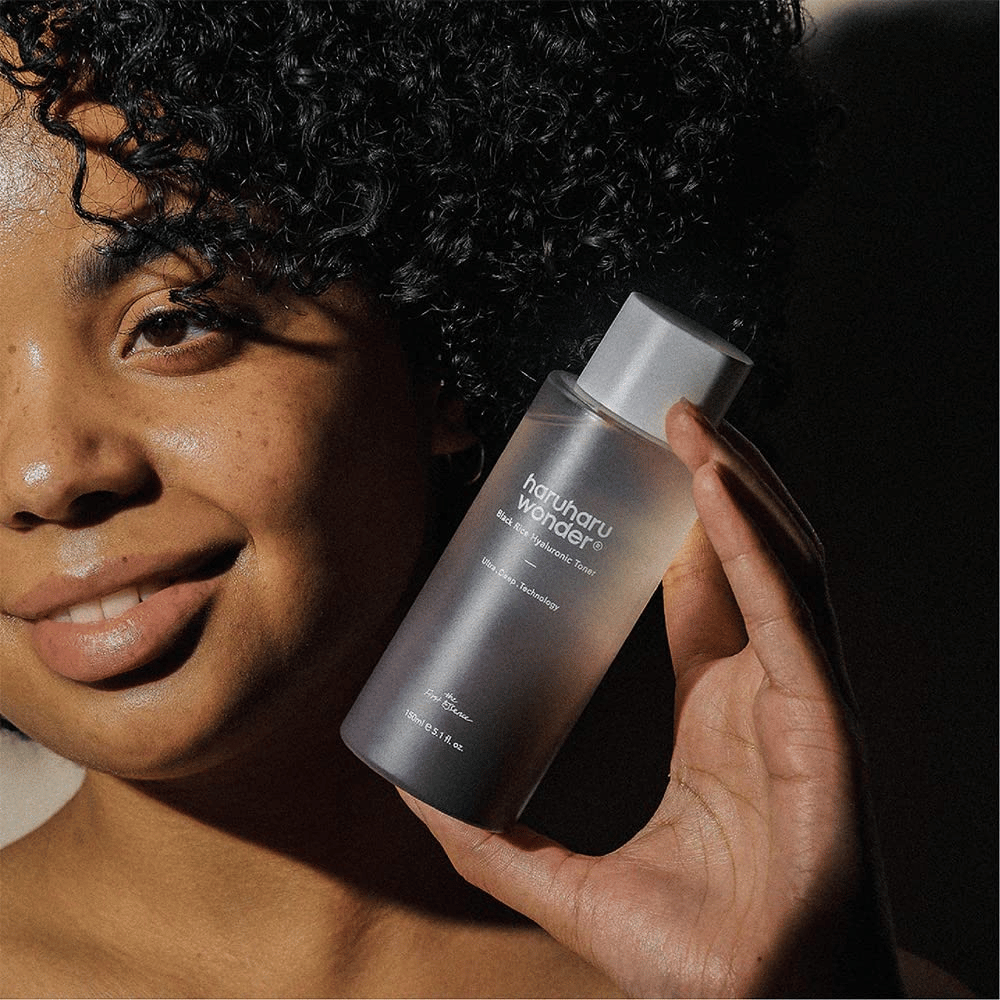 A woman holding up a bottle of Haruharu Wonder Black Rice Hyaluronic Toner Original 150ml.